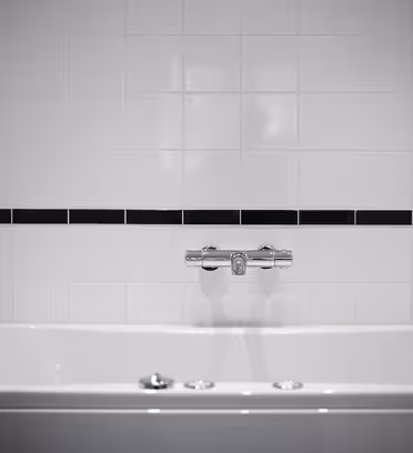 Et moderne hvidt badeværelse med blanke hvide fliser og en enkelt vandret sort stribe. En sølvhane strækker sig over et hvidt badekar og skaber et minimalistisk og rent look.